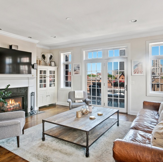 Living room with a stone fireplace, balcony doors, and views of nearby city buildings.